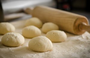 7 balls of pizza dough and a rolling pin sitting on a floured surface.