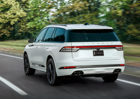 A white 2025 Lincoln Aviator® SUV is being driven away down a road lined with colorful trees. | Oliver Lincoln in Plymouth IN