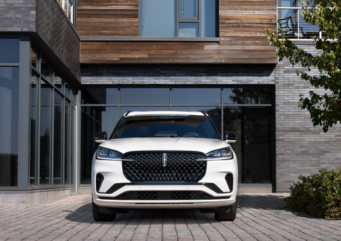 A white 2025 Lincoln Aviator® SUV is shown parked outside a modern building with gray brick and wood accents. | Oliver Lincoln in Plymouth IN