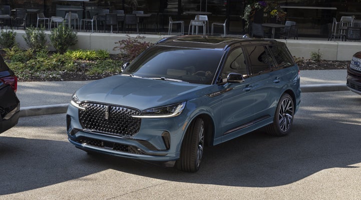 A Whisper Blue 2025 Lincoln Aviator® SUV is parked outside a modern building showcasing the driver’s side of the vehicle. | Oliver Lincoln in Plymouth IN