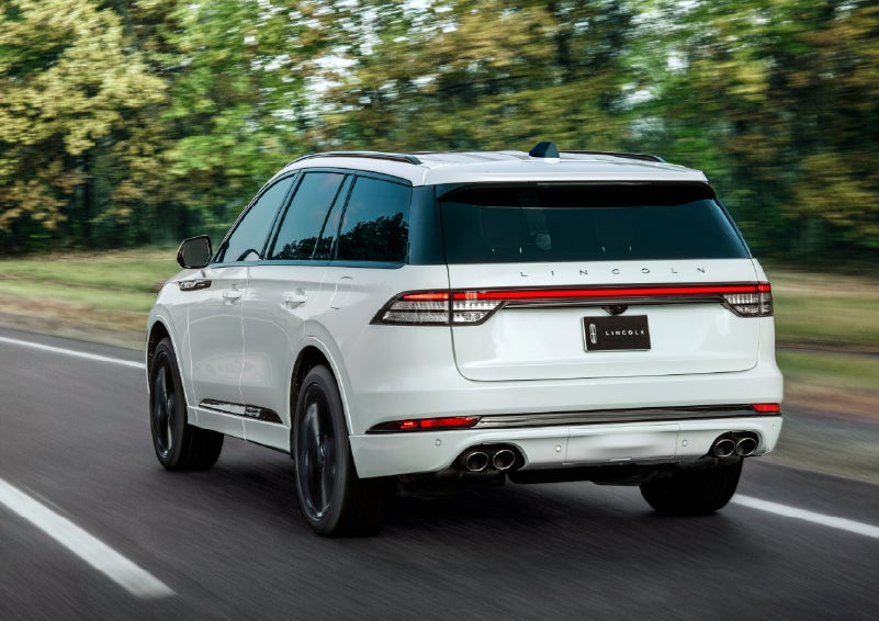 A white 2026 Lincoln Aviator® SUV is being driven away down a road lined with colorful trees. | Oliver Lincoln in Plymouth IN