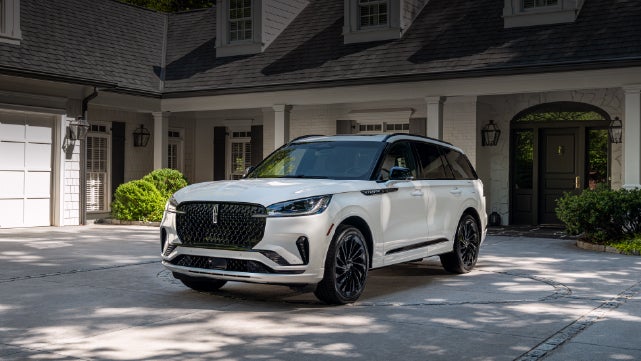 A white 2026 Lincoln Aviator® SUV is parked in the driveway of a luxury home. | Oliver Lincoln in Plymouth IN