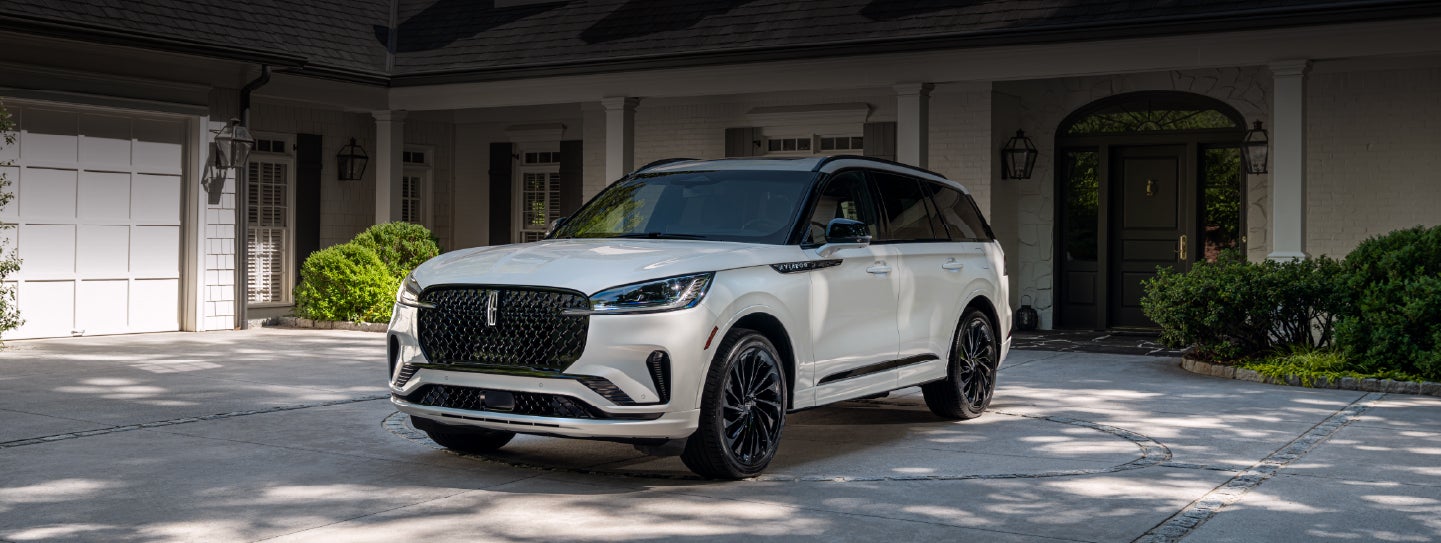A white 2026 Lincoln Aviator® SUV is parked in the driveway of a luxury home. | Oliver Lincoln in Plymouth IN