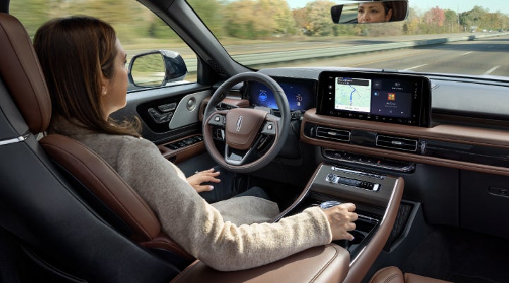 A 2027 Lincoln Aviator® SUV is being driven hands-free on a highway lined with trees. | Oliver Lincoln in Plymouth IN