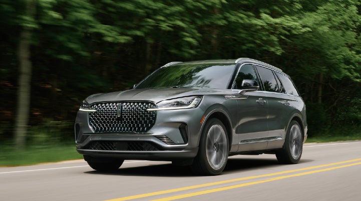 A 2027 Lincoln Aviator® SUV is being driven down a road lined with trees. | Oliver Lincoln in Plymouth IN