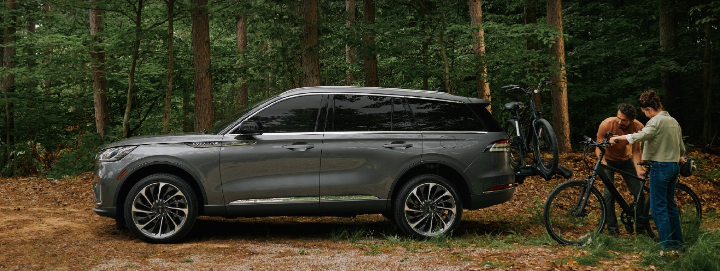 A father and son load e-bikes on a bike rack attached to a 2027 Lincoln Aviator® SUV. | Oliver Lincoln in Plymouth IN